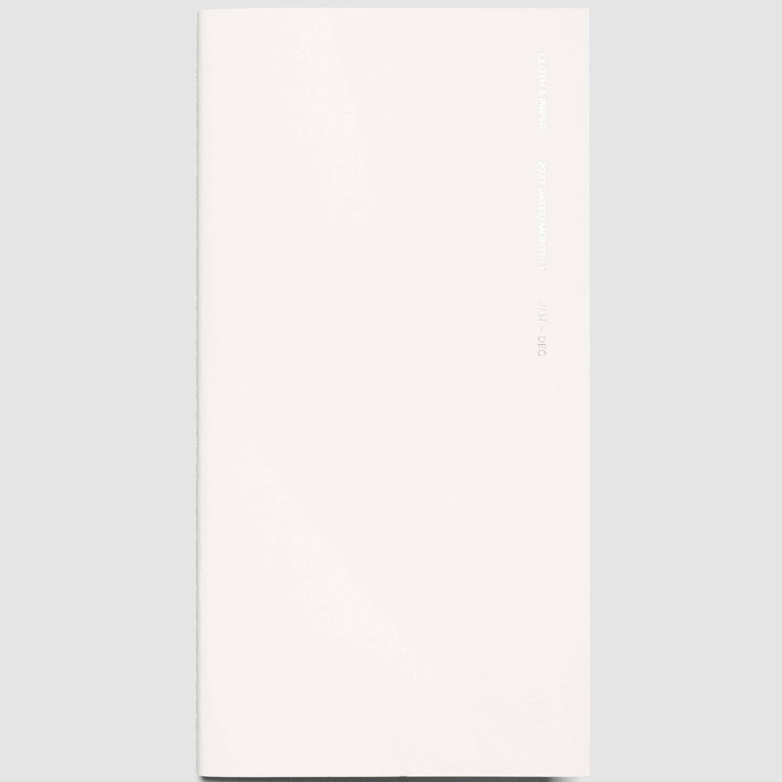 A minimalist off-white planner or journal with a glossy cover, shown vertically against a solid light gray background.