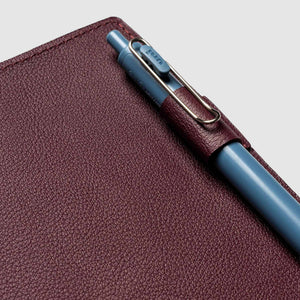 Maroon leather notebook with a blue pen on a light gray background