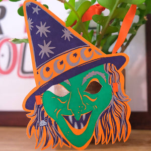 Halloween-themed mask with a purple hat and green face on a wooden surface.
