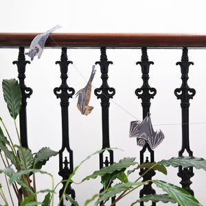 Decorative paper bats hanging from a railing with plants in the foreground.