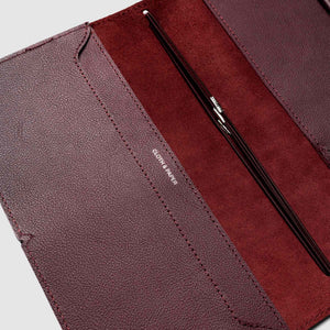 Close-up of a maroon leather wallet with a pen inside on a light gray background