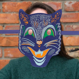 Person wearing a colorful cat mask against a brick wall