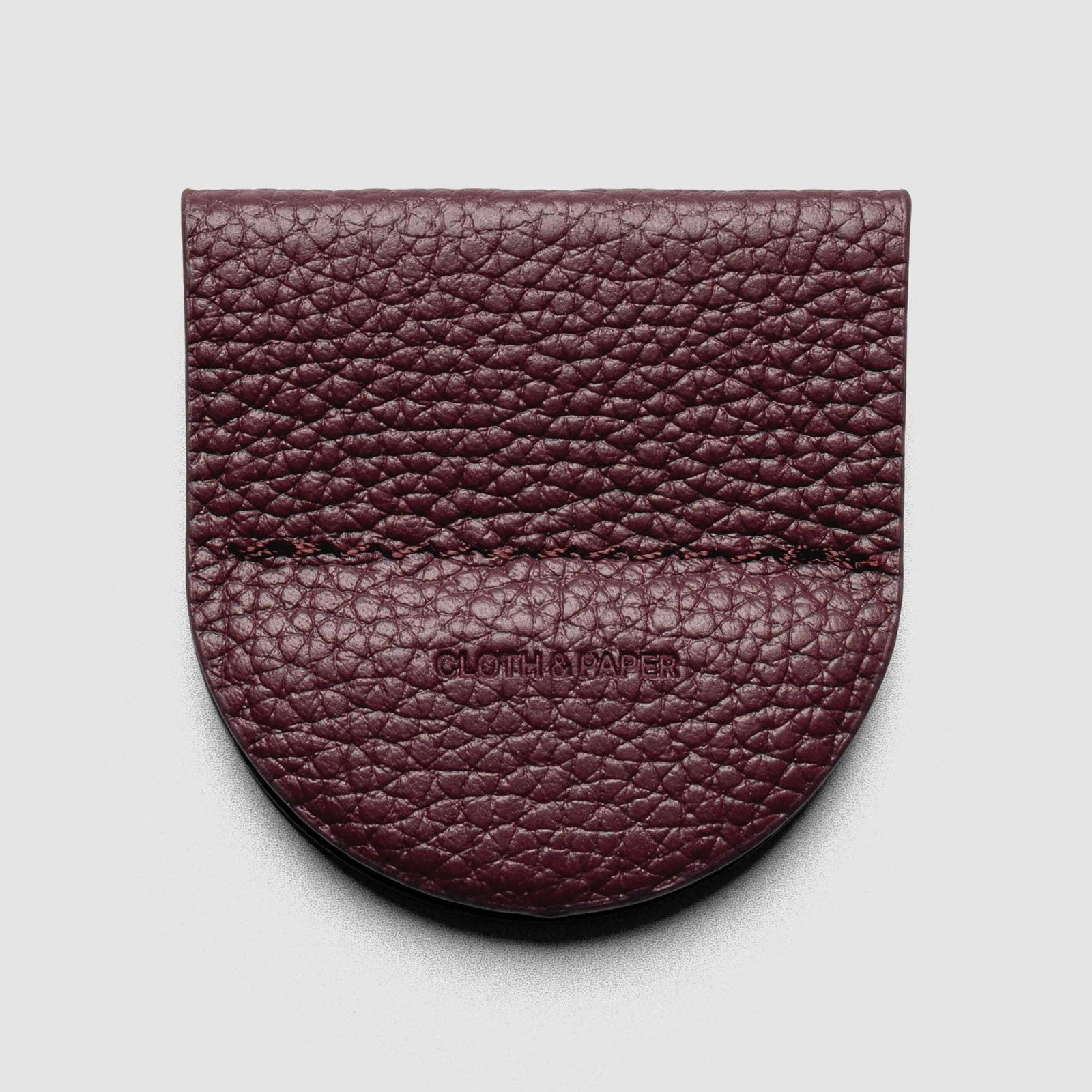A burgundy pebbled leather card holder or wallet with a rounded bottom edge and a stitched seam, featuring the embossed brand name 'CLOTHING' in the center, shown on a light gray background.