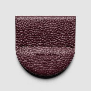 A burgundy pebbled leather card holder or wallet with a rounded bottom edge and a stitched seam, featuring the embossed brand name 'CLOTHING' in the center, shown on a light gray background.