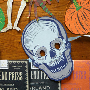 Halloween-themed cutout with a skull design on a wooden surface with pumpkins and a skeleton.