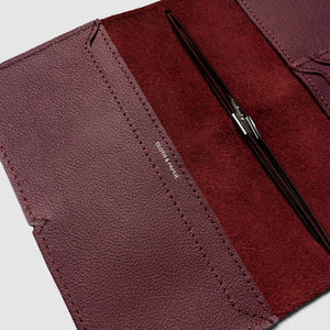 Close-up of a maroon leather wallet with a pen inside on a light gray background